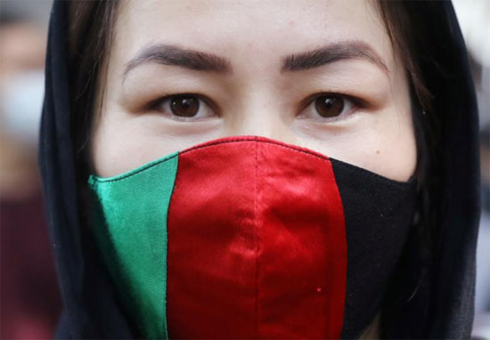 امرأة أفغانية ترتدي قناعًا بألوان العلم الوطني لأفغانستان تنظر خلال احتجاج خارج مكتب مفوضية الأمم المتحدة.