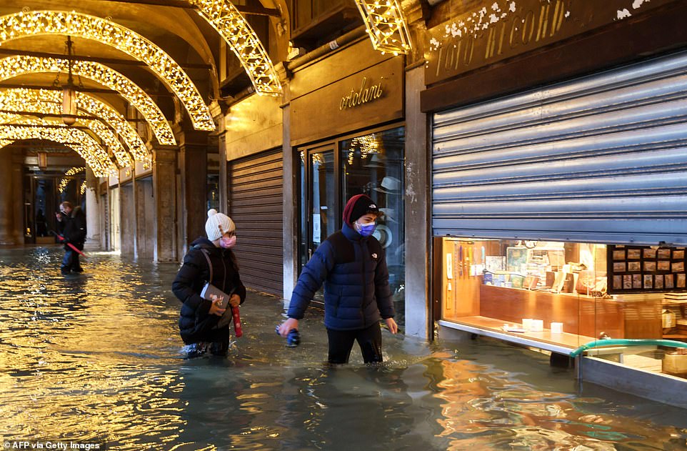 سياح يتجولون أمام المحال التجارية رغم مياه الفيضانات المرتفعة