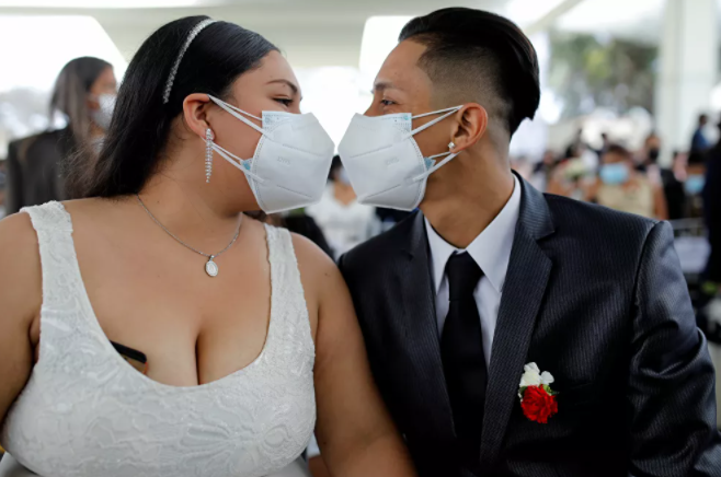قبلة زوجين حديثين وهما يرتديان كمامة خلال أول حفل زفاف جماعي منذ ظهور جائحة فيروس كورونا