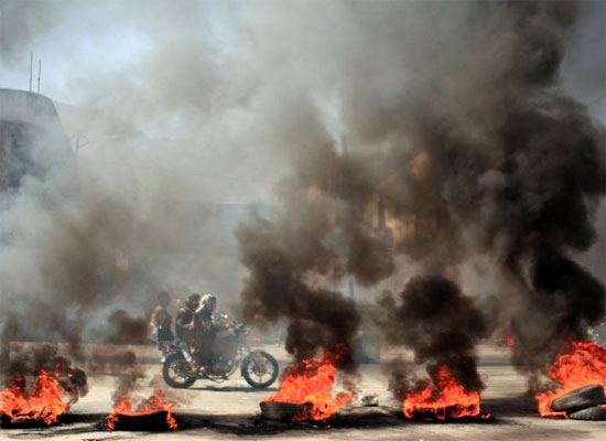 أشخاص يركبون دراجة نارية أمام الإطارات المحترقة خلال احتجاجات على تدهور الوضع الاقتصادي وانخفاض قيمة العملة المحلية