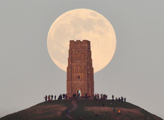 أشخاص يقفون بجانب برج سانت مايكل وهم يشاهدون ارتفاع القمر الذئب خلف جلاستونبري تور في  بريطانيا