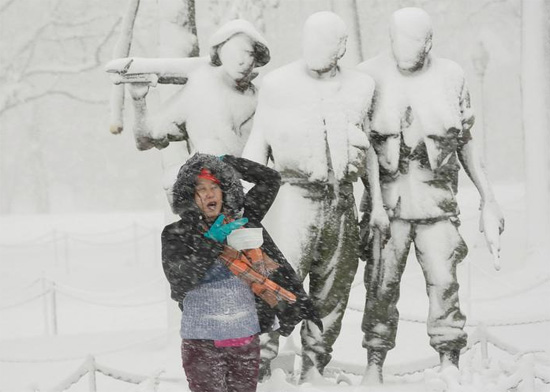 امرأة تقف لالتقاط صورة فوتوغرافية تحت تمثال مغطى بالثلوج في النصب التذكاري لقدامى المحاربين