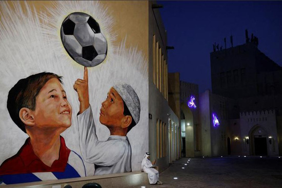 رجل يجلس بجانب لوحة جدارية لكرة القدم على جدران قرية كتارا الثقافية قبل كأس العالم