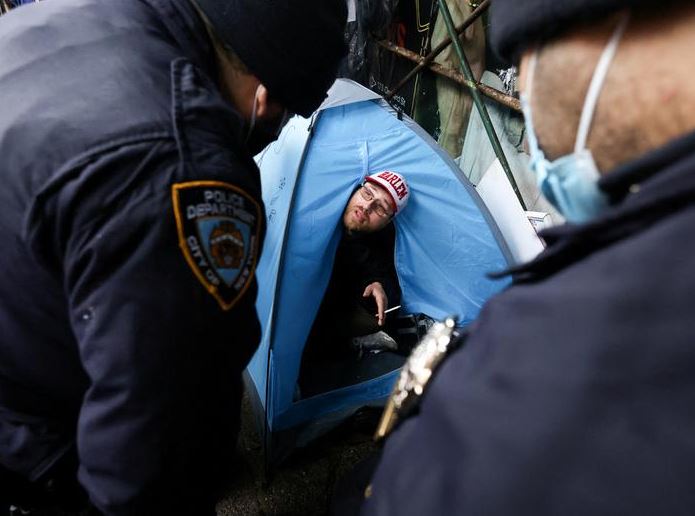 ضباط إدارة شرطة مدينة نيويورك يتحدثون إلى أحد سكان مخيم للمشردين في خيمته في شارع إيست 9 في مانهاتن ، مدينة نيويورك ، 6 أبريل  نيسان. رويترز  أندرو كيلي