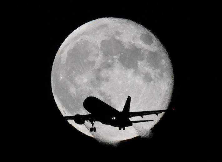 طائرة تمر أمام القمر أثناء اقترابها من الهبوط في مطار هيثرو في لندن ، بريطانيا
