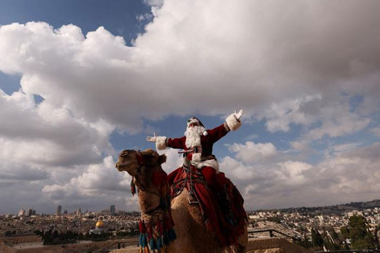 عيسى قسيسية يرتدي زي بابا نويل وهو يمتطي جمل خلال موسم عيد الميلاد على جبل الزيتون في القدس