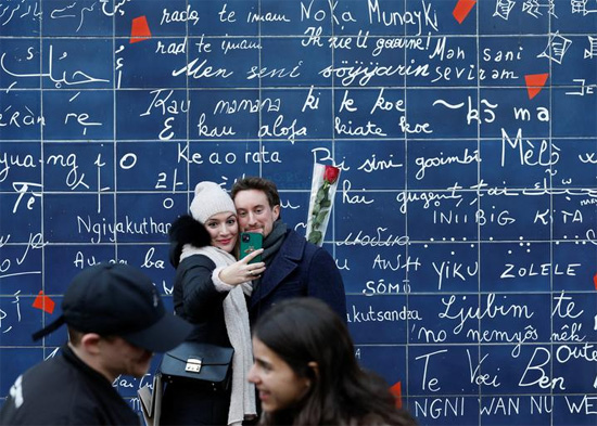 زوجان يلتقطان صورة أمام جدار الحب في ساحة حديقة جيهان ريكتوس في باريس