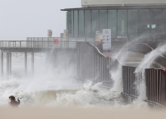 أشخاص يلتقطون صوراً بينما تتكسر الأمواج على الشاطئ في أعقاب العاصفة يونيس في بلجيكا