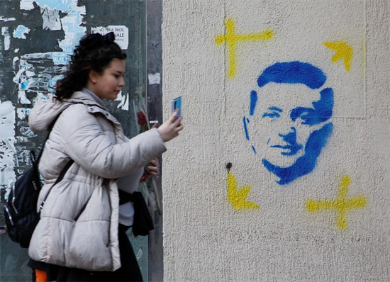 امرأة تستخدم هاتفًا أمام لوحة جدارية عليها صورة الرئيس الأوكراني