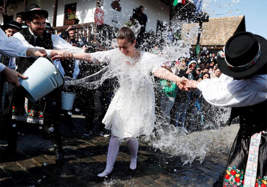 امرأة ترتدي ملابس تقليدية تتفاعل مع قيام الرجال برمي الماء عليها خلال احتفال تقليدي بعيد الفصح في المجر
