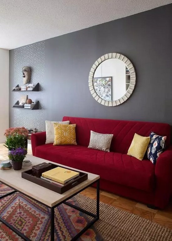 غرفة معيشة تتميز بجدار رمادي وأريكة حمراء عميقة مع وسائد ملونة وسجادة مطبوعة