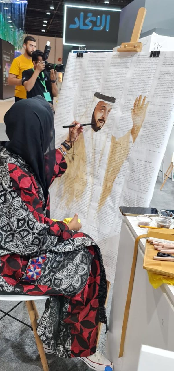 علياء البازعى ترسم الشيخ خليفة بن زايد بالقهوة فى معرض أبوظبى للكتاب