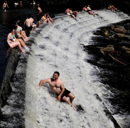 الناس يسترخون في نهر ديروينت في أراضي منزل تشاتسوورث خلال موجة الحر ببريطانيا