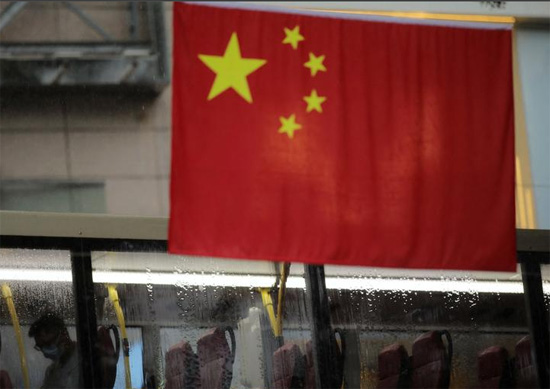 حافلة تسير أمام العلم الصيني تحت المطر