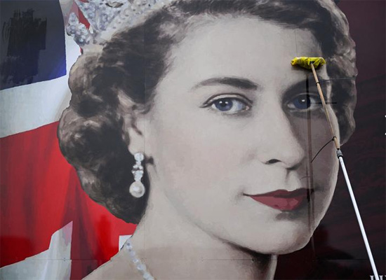 شخص يضع لوحة إعلانية تصور ملكة بريطانيا إليزابيث