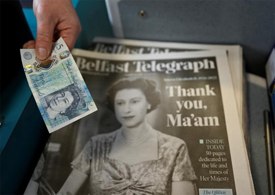 شخص يحمل نقودًا فوق صحيفة عليها صورة ملكة بريطانيا إليزابيث