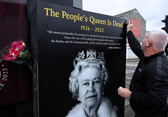 رجل يضع لوحة تصور الملكة إليزابيث ملكة بريطانيا في بلفاست أيرلندا الشمالية