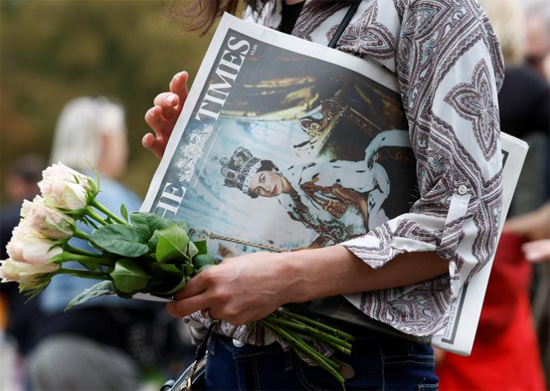 امرأة تحمل زهورًا وصحيفة تصور الملكة إليزابيث ملكة بريطانيا في قلعة وندسور