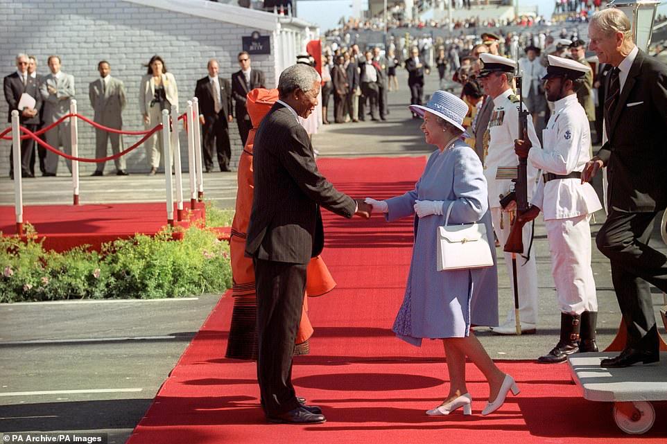 رئيس جنوب أفريقيا نيلسون مانديلا يحيي الملكة إليزابيث الثانية وهي تخطو من اليخت الملكي بريتانيا في كيب تاون في 20 مارس 1995 في البداية الرسمية لأول زيارة