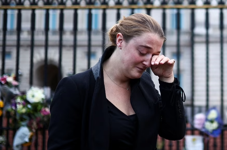 امرأة تذرف الدموع بعد أن ألقت زهور امام قصر باكنغهام