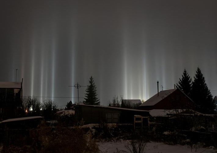 تبرز أعمدة الضوء ، وهي ظاهرة بصرية في الغلاف الجوي ، من الأرض إلى السماء خلف المباني السكنية في أومسك ، روسيا