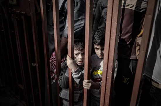 أطفال غزة يقفون خلف بوابة حديدة تشبه القضبان دلالة عن حبس حريتهم 