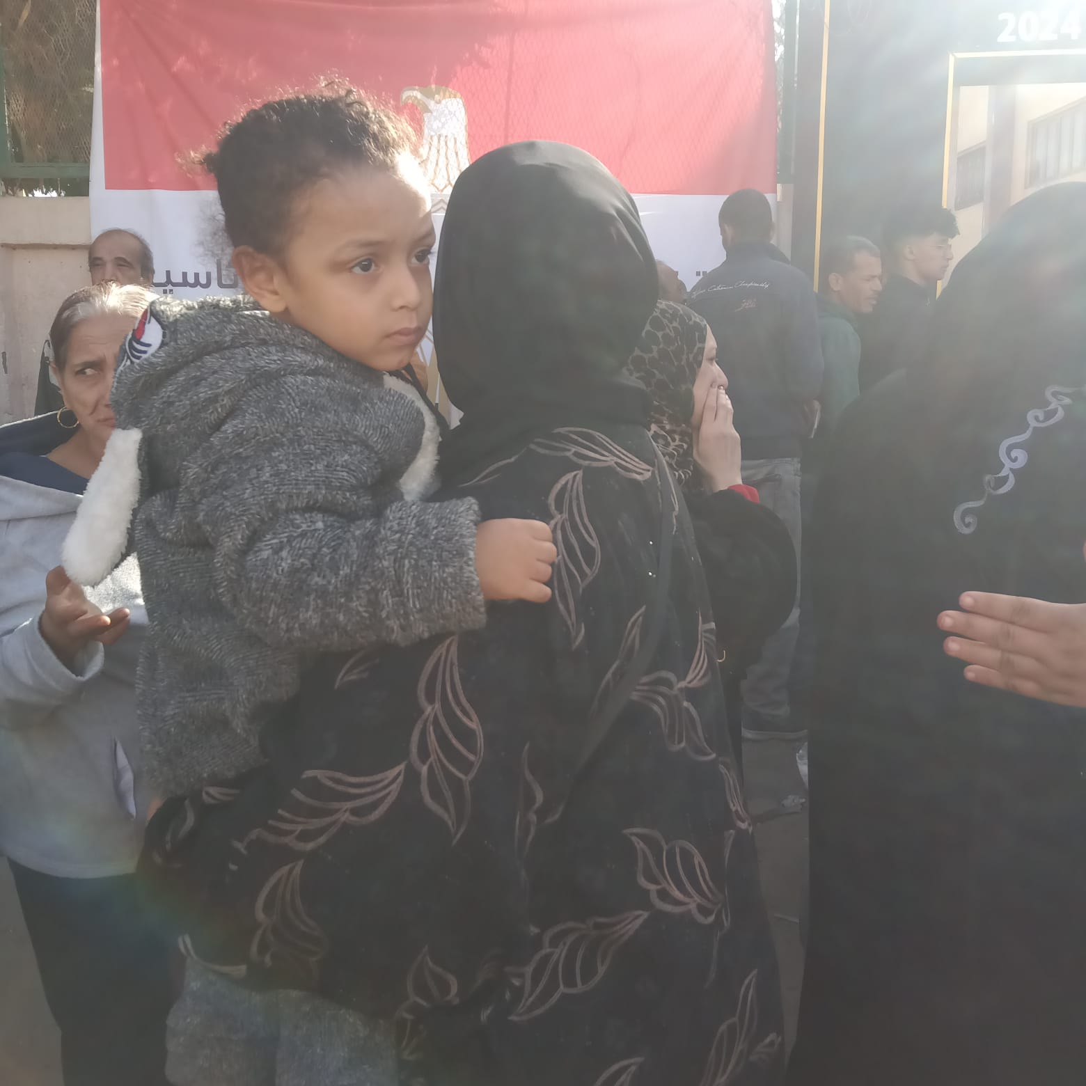 سيدة تحمل ابنتها أثناء توجهها للإدلاء بصوتها الانتخابي