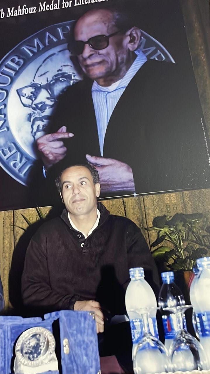 حمدي أبو جليل مع صورة نجيب محفوظ في حفل فوز روايته الفاعل