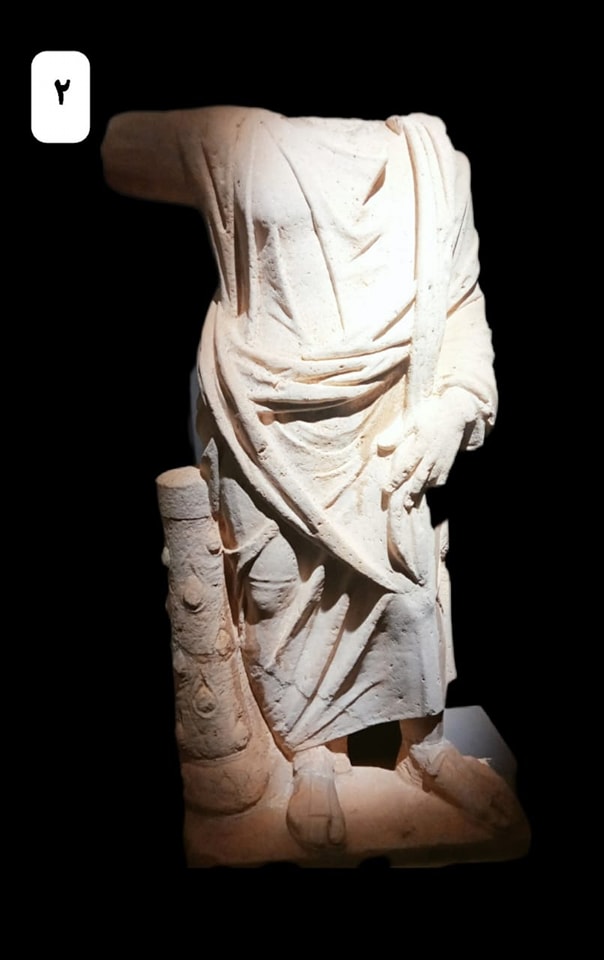 تمثال لسرابيس بهيئة رجل واقف يحمل صولجان مفقود في يمناه ويرتدي عباءة وقميص وصندل يرجع للعصر الروماني