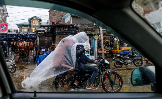 رجال كشميريون يحتمون تحت غطاء من البوليثين لحماية أنفسهم من هطول الأمطار