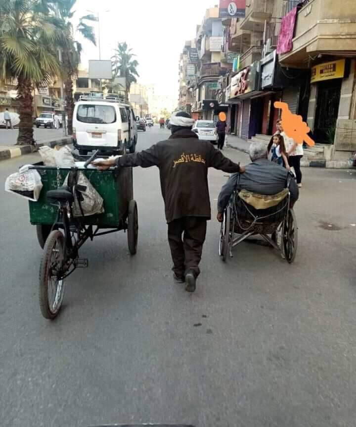 صورة اليوم عامل بشارع التليفزيون بالأقصر يساعد مسن على كرسي متحرك