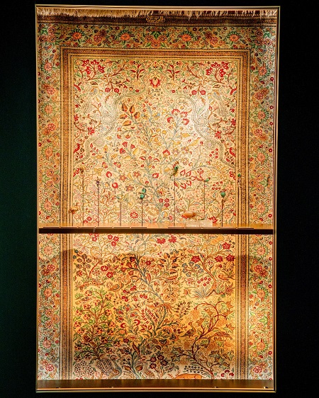 واجهة عرض للمجوهرات وفي الخلفية سجادة منقوشة برسوم الطيور