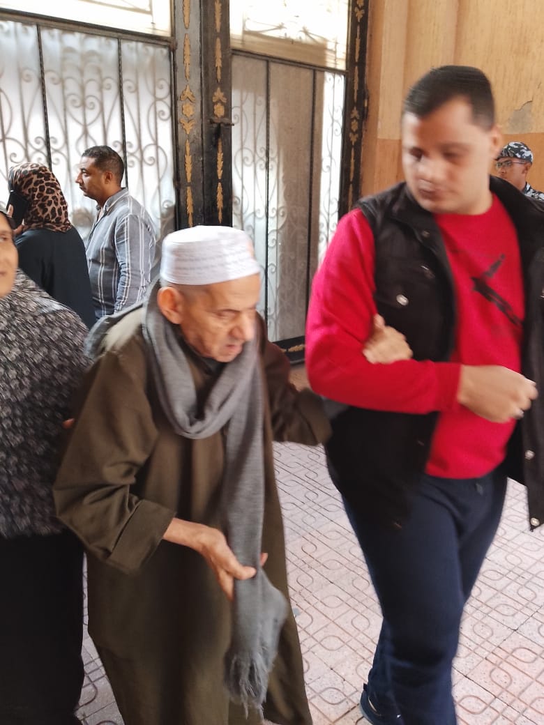 موظف يساعد ناخب مسن لدخول اللجنة الانتخابية بالمطرية