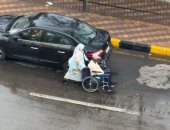 زوجة تدفع زوجها على كرسي متحرك أسفل الأمطار