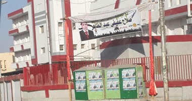 مرشح انتخابى يعلق لافتة دعائية على سور مستشفى أسوان الجامعى