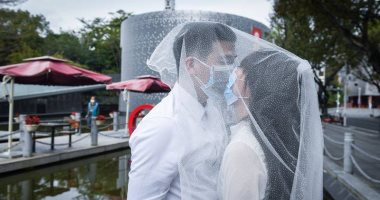 رغم أنف كورونا..قبلات متبادلة "بالكمامات" لعروسين بعد تسجيل زواجهما بالصين