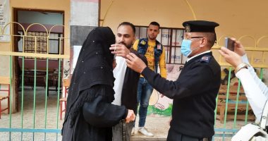 شرطى يساعد سيدة مسنة على ارتداء الكمامة أمام لجنة انتخابية بالفيوم.. صور