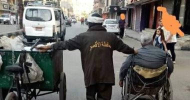 عيد العمال.. صورة لرجل نظافة بشارع التليفزيون بالأقصر يساعد مسنا على كرسى متحرك
