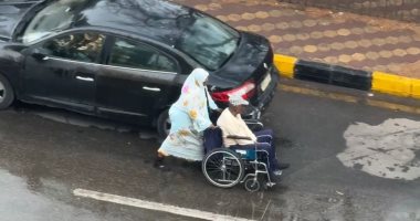 زوجة تدفع زوجها على كرسي متحرك أسفل الأمطار