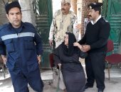 رجال الشرطة يعاونون سيدة مسنة فى الوصول إلى لجنتها بأرض اللواء