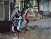 شاب يحمل سيدة عجوز لعبور الطريق بعد غرقها بمياه الأمطار بالغربية.. صور