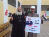 شيخ وقس يرفعان لافتة تدعو الناخبين للمشاركة فى الانتخابات البرلمانية بالمنيا