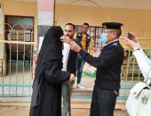 شرطى يساعد سيدة مسنة على ارتداء الكمامة أمام لجنة انتخابية بالفيوم.. صور