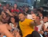 تامر حسني يخرج من سقف سيارته لالتقاط الصور مع محبيه قبل حفل الساحل.. فيديو 