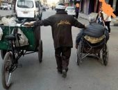 عيد العمال.. صورة لرجل نظافة بشارع التليفزيون بالأقصر يساعد مسنا على كرسى متحرك