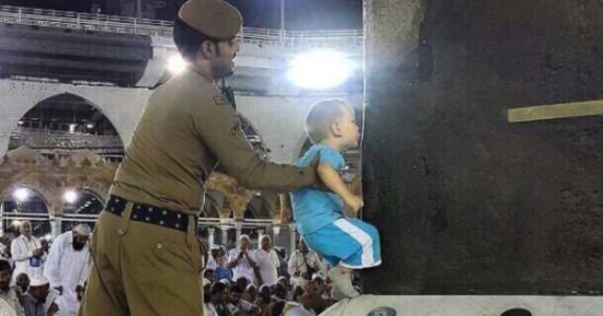 بالصور.. رجل أمن سعودى يساعد طفلا فى تقبيل الكعبة الشريفة