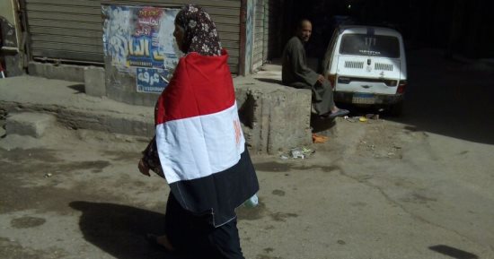 عجوز ترتدى علم مصر وتجوب شوارع فيصل لحث المواطنين على المشاركة بالانتخابات