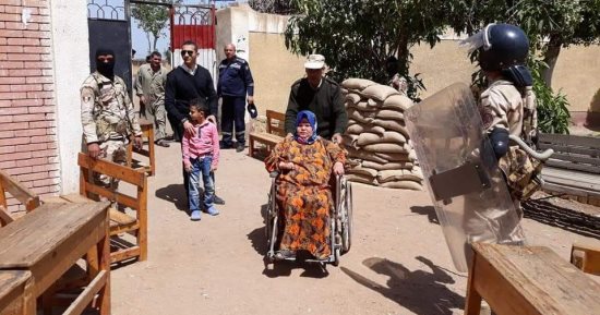 صور.. مجند يساعد سيدة معاقة للإدلاء بصوتها فى الانتخابات بالقليوبية