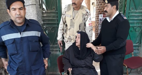 رجال الشرطة يعاونون سيدة مسنة فى الوصول إلى لجنتها بأرض اللواء