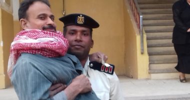 صور.. أمين شرطة بسوهاج يحمل مريضا للجنته بالطابق الثالث للمشاركة بالاستفتاء